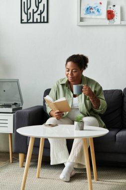 Rahat bir kadın, en sevdiği kitabın tadını çıkarırken modern, davetkar ortamında çayını yudumluyor..