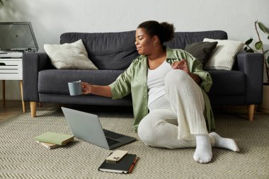 Afro-Amerikalı bir kadın evinde dizüstü bilgisayarına odaklanırken rahatlıyor..