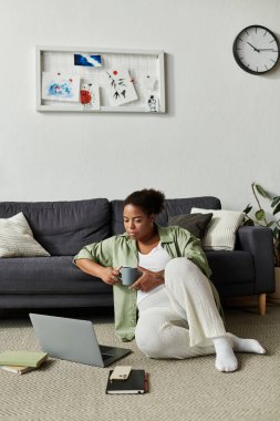 Odaklanmış kadın sıcak bir içkinin keyfini çıkarırken rahat bir dairede çalışıyor..