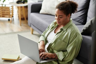 Afrikalı Amerikalı bir kadın, evde çalışırken bilgisayarını karıştırıyor..