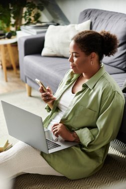 Afrika kökenli Amerikalı bir kadın yerde rahatça otururken uzaktan kumandayla meşgul oluyor..