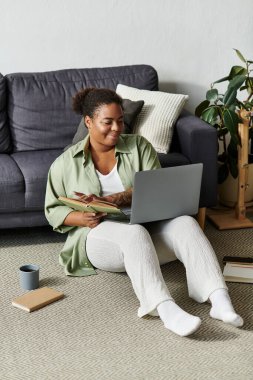 Afrikalı bir Amerikalı kadın yerde otururken günlük kıyafetlerle uzaktan çalışmaktan hoşlanır..