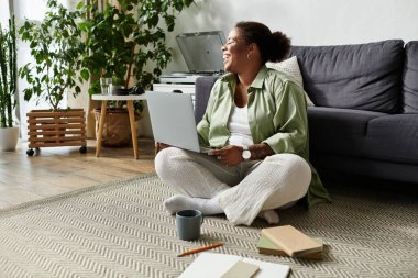 Afro-Amerikalı bir kadın evinde yerde oturmuş laptopuyla uğraşıyor..