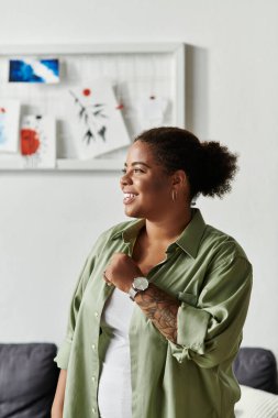 Neşeli bir kadın günlük giysiler içinde gülümseyerek ve yansıtarak rahat dairesinden zevk alır..