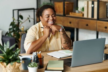 Neşeli bir siyahi kadın, şık bir dairede dizüstü bilgisayarıyla çalışırken gülümsüyor..