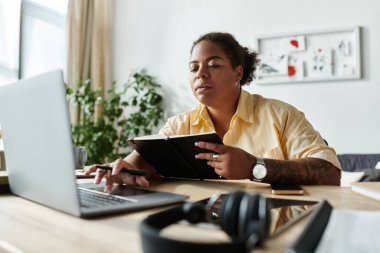 Sıradan giyinmiş Afrikalı bir Amerikalı kadın evinde dizüstü bilgisayarla işine konsantre oluyor..