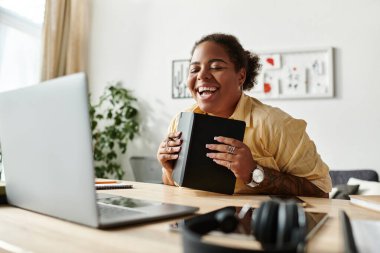 Afrika kökenli Amerikalı bir kadın ev masasında dizüstü bilgisayarla çalışırken yaratıcılığı kucaklıyor..