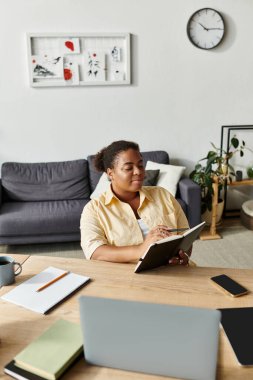 Afrikalı bir Amerikalı kadın masasında özenle çalışıyor, sıcak evindeki işleri dengeliyor..