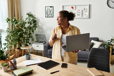 Afro-Amerikalı bir kadın şık dairesinden, laptopunu açıp notlar alarak çok çalışıyor..