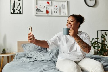 Afro-Amerikalı bir kadın sıcak bir içki ve yatağında bir gülümsemeyle sabahının tadını çıkarıyor..