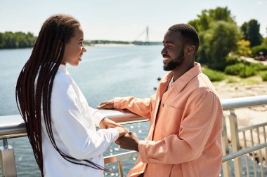 Sevgi dolu çiftler su kenarında el ele dolaşır, gülüşlerini ve güneşte olan bağlantılarını paylaşırlar.