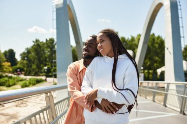 Sevgi dolu çift, güzel güneşli bir günde parkta bir köprüde yürürken birbirlerini kucaklarlar..