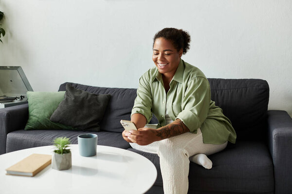 Женщина наслаждается случайным днем дома, погруженная в телефон и улыбающаяся от радости.