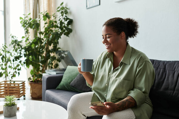 Афроамериканка наслаждается чашечкой чая, расслабившись на диване в стильной гостиной.