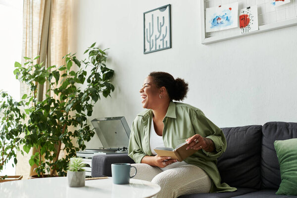 В теплой и уютной квартире веселая женщина наслаждается своей книгой, наслаждаясь напитком.