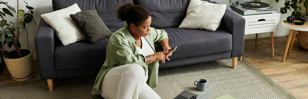 An African American woman works remotely on the floor, surrounded by home decor, banner