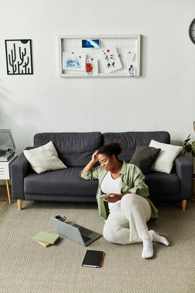 An African American woman in casual attire engages in remote work while seated comfortably.