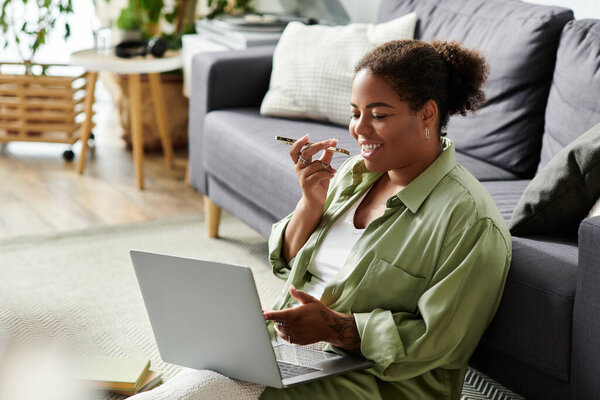 A young woman is engaged in remote work, happily using her laptop while sitting on the floor.