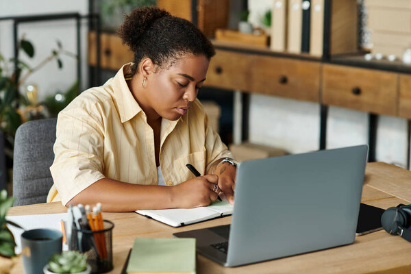 Афроамериканка сосредоточена на своей работе, сидя за столом в своей квартире..