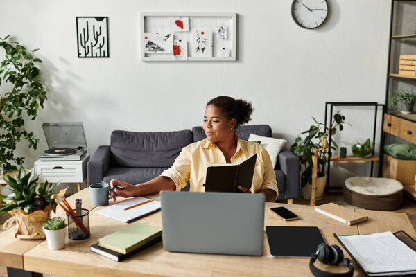 An African American woman in casual clothes sits at her desk working while enjoying a drink.