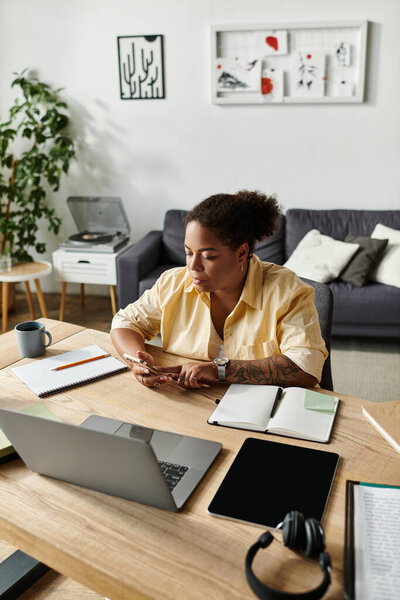 African American woman in casual attire sits at her desk, engaged in remote work activities.