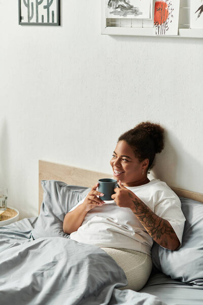 An african american woman enjoys her morning routine with a warm drink in a stylish bedroom.