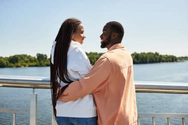 Sevgi dolu bir çift, suyun kenarında yürürken birbirlerine sarılır ve gülümserler..