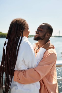 Genç çiftler nehir kenarında dolaşır, sıcacık güneşin altında sarılır ve gülerler..