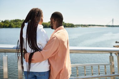 Genç bir çift, güneşli bir günde nehir kenarında romantik bir yürüyüş yaparken kucaklaşır..