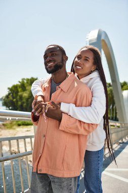 Sevgi dolu çift el ele yürür manzaralı bir yolda, birbirlerine gülümseyerek sarılırlar..