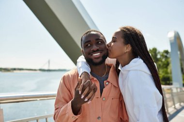 Nehir kenarında neşeli bir çift gezintisi, güneşin altında kahkaha ve şefkat paylaşıyor..