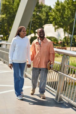 Sevgi dolu çift, yeşil ve şehir hayatı ile çevrili modern bir köprü boyunca el ele yürür..