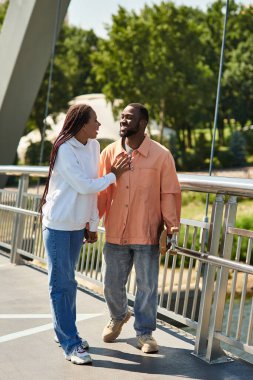 İki aşık el ele yürür manzaralı bir köprüde, sevginin ve doğanın tadını çıkarırlar..
