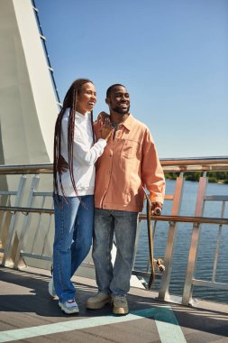 Genç bir çift rıhtım yolunda mutlu bir şekilde yürüyor, gülüşmeler ve kahkahalar paylaşıyor..