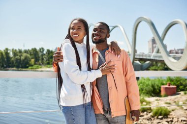Sevgi dolu bir çift, doğa ve şehir manzarasıyla çevrili nehir boyunca yürürken kucaklaşır..