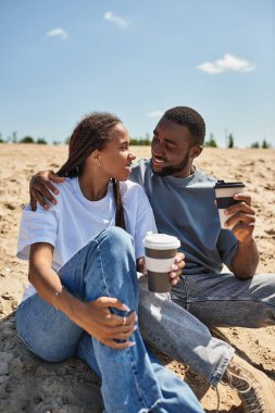 Bir çift gülüyor ve açık gökyüzünün altında yumuşak kumlarda içmekten hoşlanıyor..