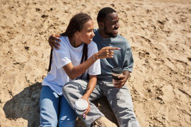 Sevgi dolu çift kumsalda rahatlar, kahve yudumlar ve güneşin altında birlikte vakit geçirirler..