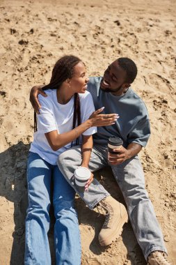 Genç çift, güneşin altındaki sıcak kumda içmeyi ve gülümsemeyi sever..