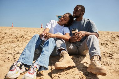 Sevgi dolu bir çift sıcak kumda rahatlar, kahvelerini yudumlar ve birlikte vakit geçirirler..