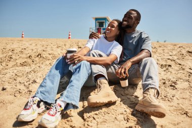 Sevgi dolu bir çift kumlu sahilde güneşlenir, gülümsemelerini ve sıcaklıklarını paylaşırlar..