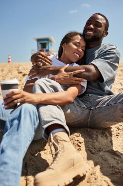 Genç ve sevgi dolu bir çift kumsalda oturur, sıcaklığını ve kahkahalarını paylaşır ve eğlenir..