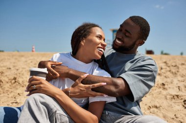 Sevgi dolu çiftler kumsalda gezerler, güneşin altında kahkahalarla ve sıcaklıkla sarılırlar..