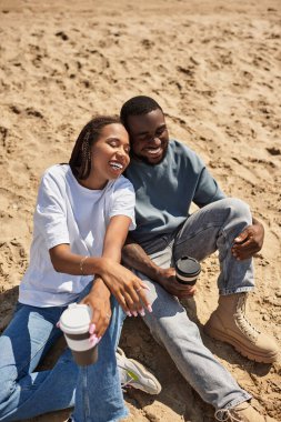Neşeli bir çift, kumlu bir sahil boyunca el ele gezerken kahkahalarını paylaşır..