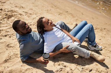 Genç çift kumsalda el ele yürür, dalgaların çarpmasıyla birlikte gülüşürler ve aşklarını paylaşırlar..