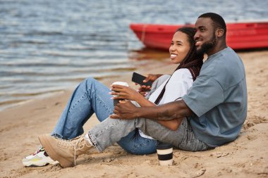 Sevgi dolu bir çift su kenarında el ele gezer, gülüşlerini ve gülüşlerini güneşin altında paylaşır..