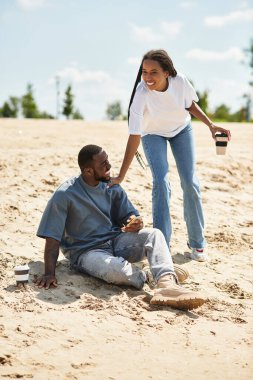 Neşeli bir çift kumlu sahil boyunca el ele gezer, sıcak güneş ışığında güneşlenirler..