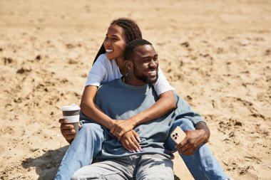 Sevgili eşler kumsalda yürürken birbirlerini mutlu bir şekilde kucaklarlar..