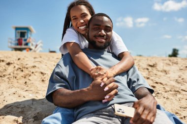 Genç çift el ele yürür, gülüşürler ve kahkahalar atarak kumsalda güneşlenirler..