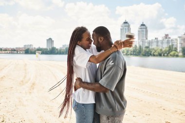 Sevgi dolu bir çift su kenarında el ele gezer, gülümsemelerini paylaşır ve sıcak bir içki içerler..