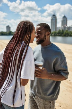 Genç çift kumlu bir sahil boyunca el ele yürürken neşeli bir anı paylaşıyor..